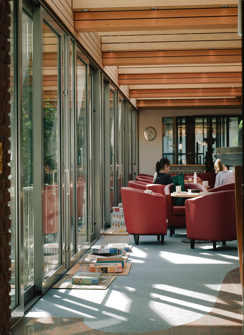 Gemütlicher Aufenthaltsraum mit roten Sesseln und großen Glasfronten in der Klinik Lüneburger Heide.