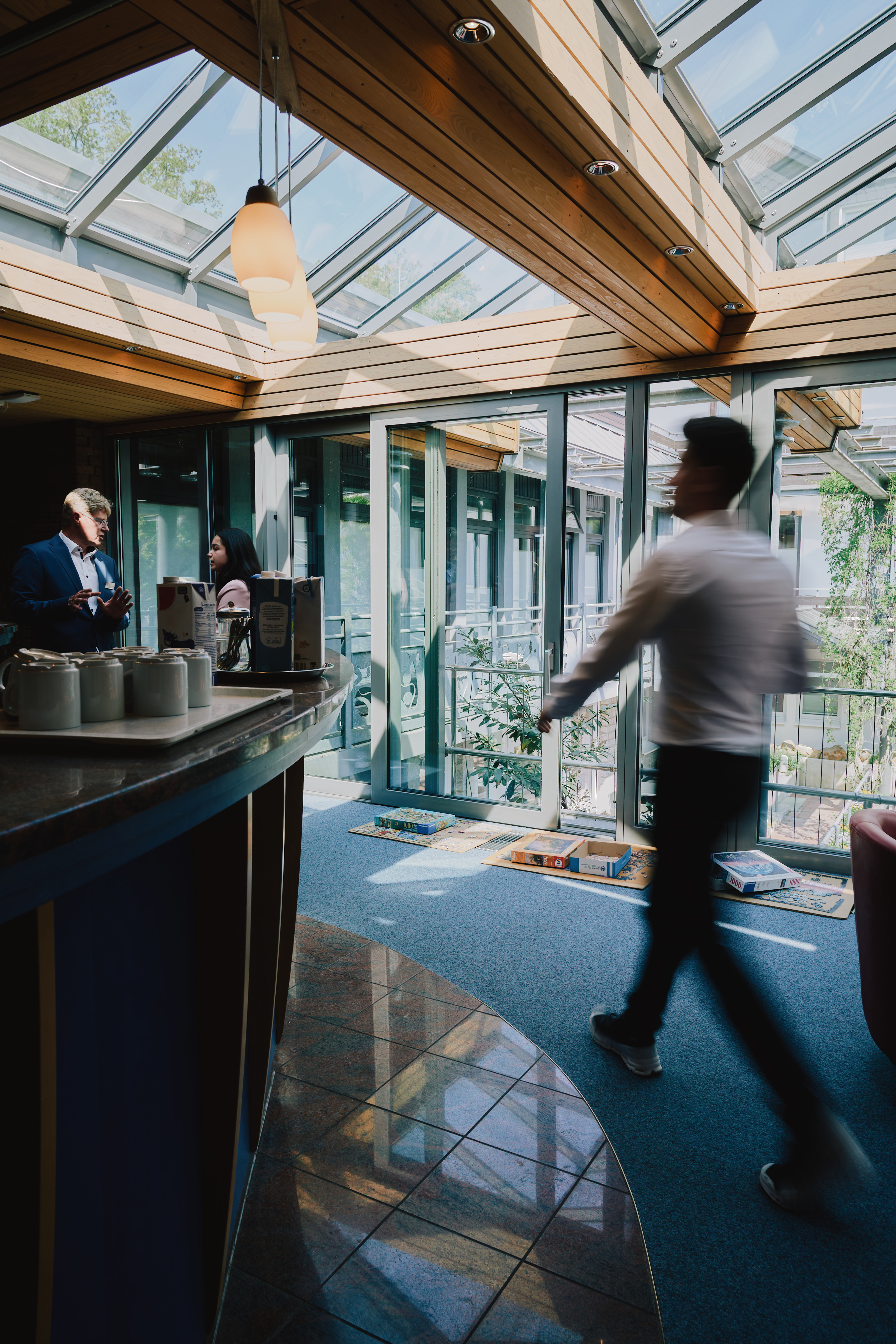 Heller Aufenthaltsbereich der Klinik Lüneburger Heide mit Glasdach und modernen Sitzgelegenheiten, in dem Mitarbeitende im Gespräch sind